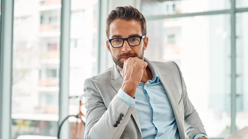 man with glasses sits thoughtfully in office