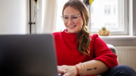 Frau sitzt mit Notebook zu Hause auf dem Sofa Hier geht es zur Newsmeldung D-Trust bietet die rein elektronische Bestellung des elektronischen Heilberufeausweises für nicht approbierte Leistungserbringer im Gesundheitswesen an.